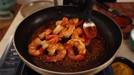 chef crushing the garlics in the boiling oil on the cooking pan with a spoon to infused the flavours in the sauteed seafood prawn dish, close up shot