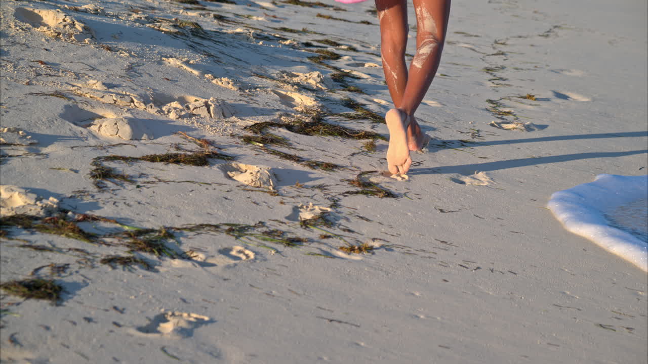 mujer delgada y bronceada caminando descalza sobre la arena dejando sus huellas en una tarde soleada en la playa