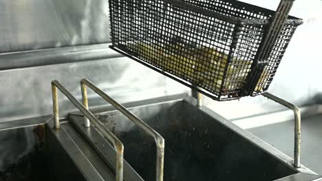 crop cook preparing french fries in deep fryer in kitchen