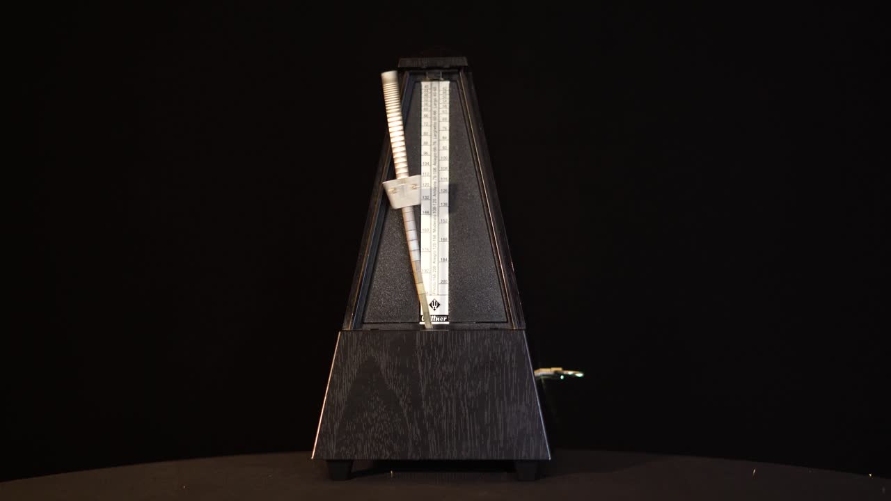 검은 화면에서 진자가 움직이는 메트로놈의 전면 보기, 리듬으로 연주되는 음악