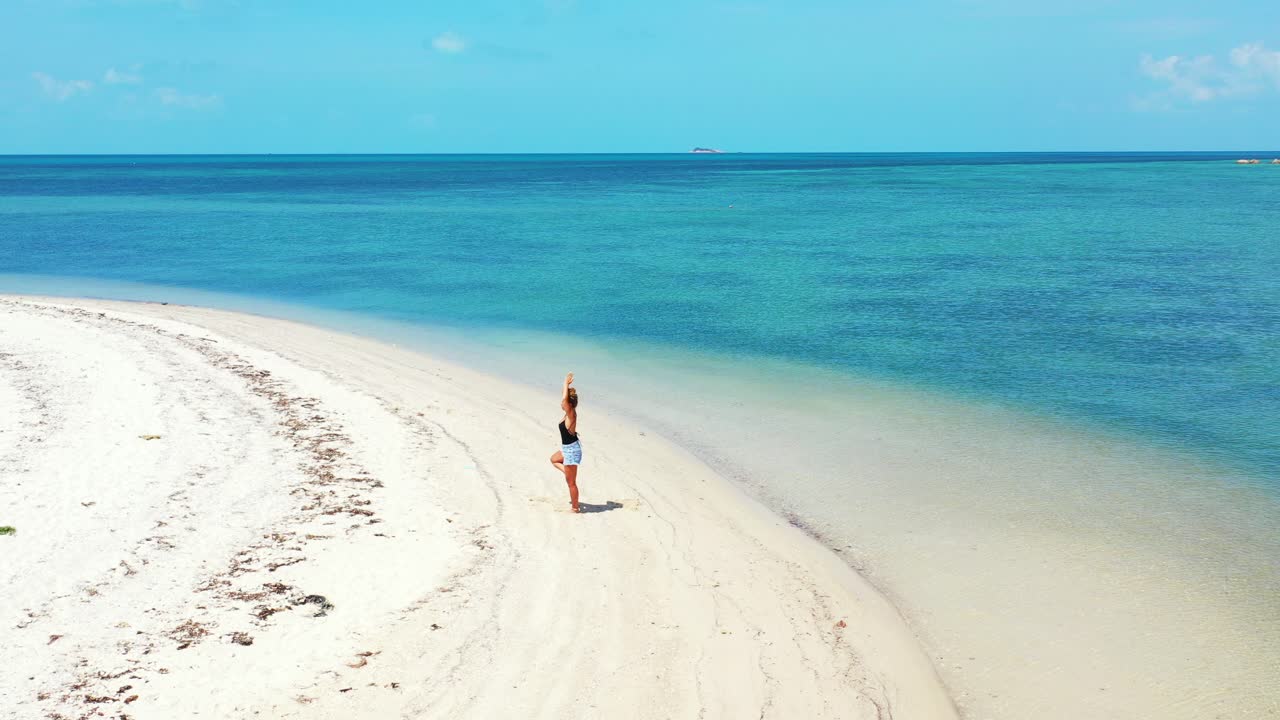 Lonely woman doing Yoga on calm exotic beach with white sand washed by blue turquoise sea at sunrise
