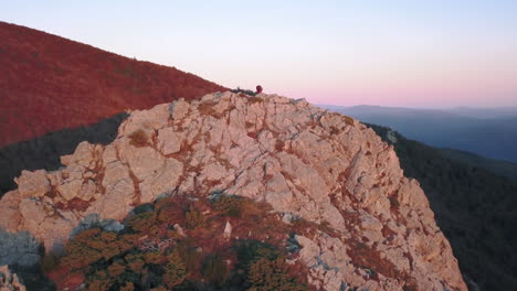 Verkleinern-Sie-Die-Drohnenaufnahme-Einer-Frau,-Die-Auf-Einem-Berg-Mit-Den-Ersten-Lichtern-Des-Sonnenaufgangs-Yoga-Macht