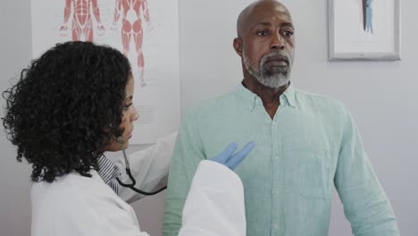 diverse female doctor examining male patient in consulting room, using stethoscope, slow motion