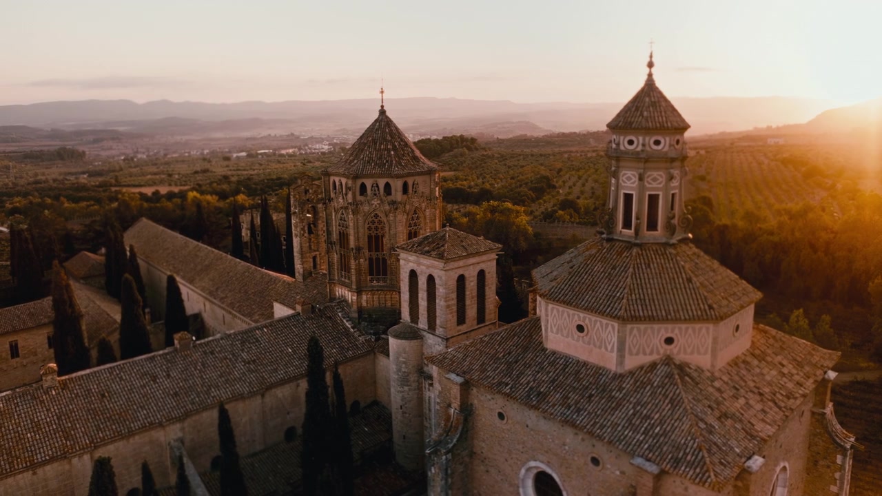 Vista aerea ravvicinata con drone del Monastero di Santa Maria de Poblet all'ora d'oro, con il suo storico campanile, tetti in tegole e la calda luce del tramonto sulla campagna catalana