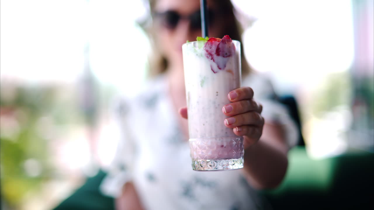 Woman presenting a strawberry drink with a black straw at a restaurant