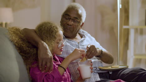 chica con abuelo comiendo galletas con leche antes de ir a la cama