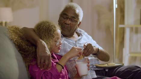 girl with grandpa having biscuits with milk before going to bed