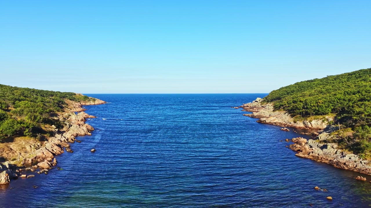 Acqua calma scorre tra coste rocciose sotto un cielo azzurro e limpido in una zona costiera.