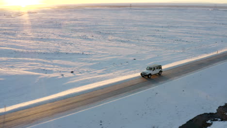 AERIAL:-Flying-besides-Jeep-on-snowy-road-in-Iceland-at-Sunset-Winter,-Sun,-Arctic