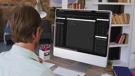 hombre caucásico sentado en un escritorio viendo el procesamiento de datos de codificación en la pantalla de la computadora