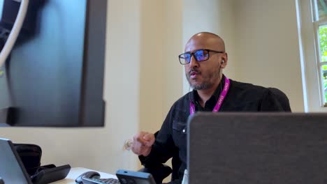 South-Asian-male-wearing-glasses,-air-drumming-at-his-desk-while-listening-to-music-in-an-office-setting