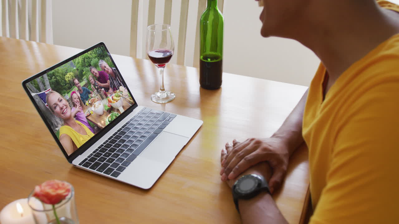Biracial man sitting at table using laptop making video call with family