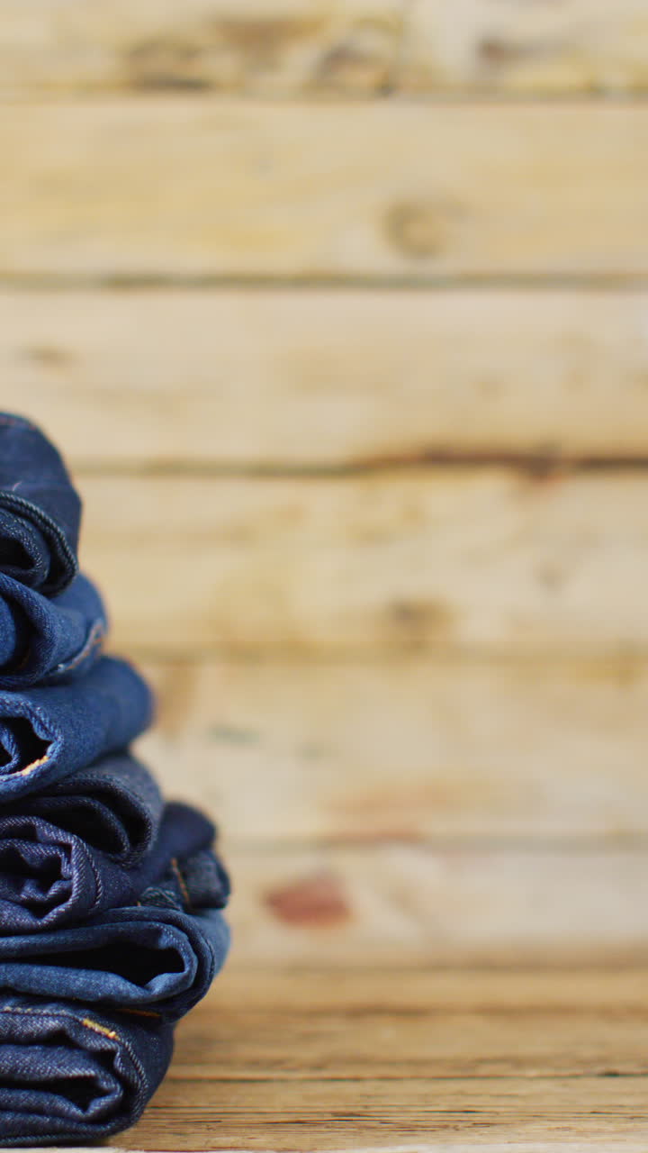 Vertical video of folded jeans with different shades on wooden background with copy space