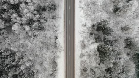 Aerial view of a two lane asphalt highway through the woods in winter. Top down drone view of an empty road in countryside.