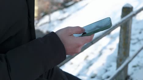 detail view of a caucasian male hand scrolling through a smartphone while outdoors during winter