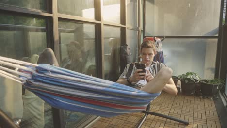 man with smartphone relaxing on a hammock in the house