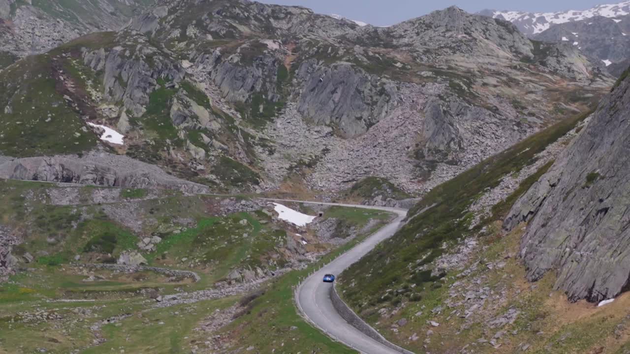 Arka planda çimenli yamaç ve kayalıklarla bir virajı dönen dağ yolu.