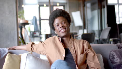 portrait of happy african american man with afro sitting on sofa at home, slow motion