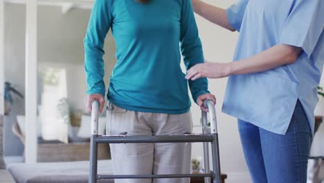 female health worker assisting senior woman to walk with walking frame at home