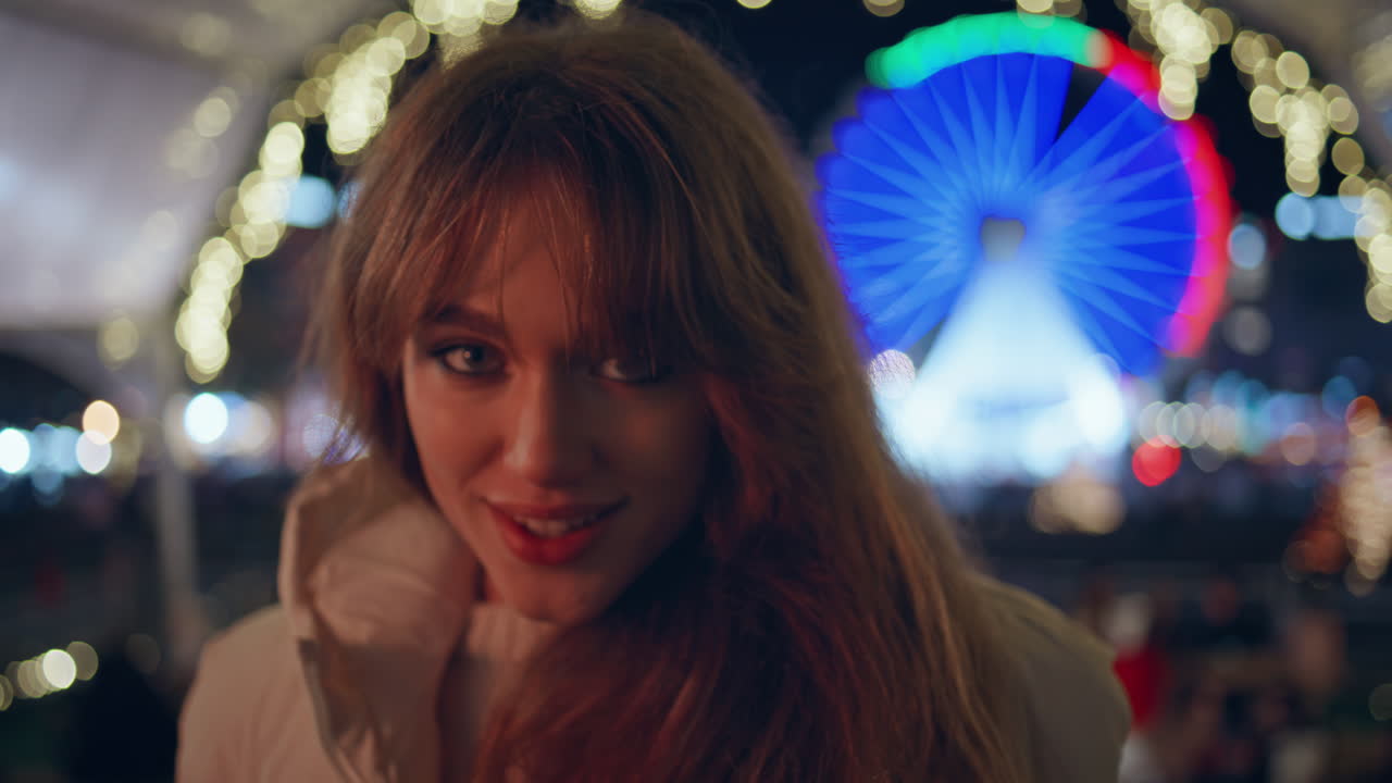 크리스마스 불빛으로 둘러싸인 축제의 박람회장을 포즈로 하고 있는 즐거운 여성.