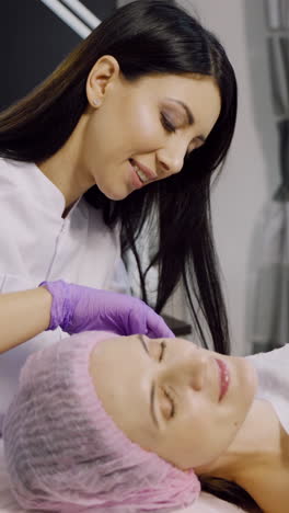 A cosmetologist makes injections for a woman in a beauty center. The client is laying on the couch during the procedure. Mesotherapy. Vertical video