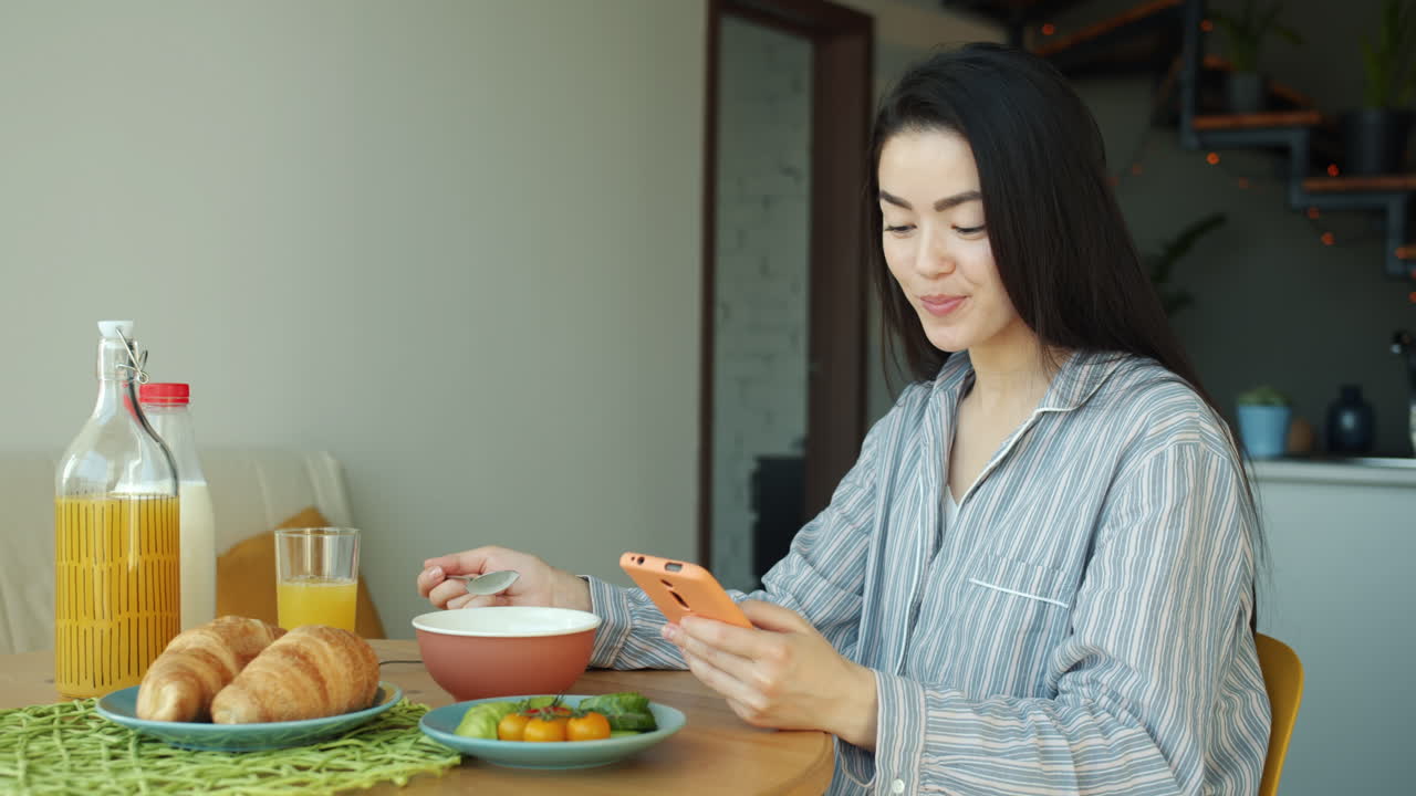 Woman eating breakfast and using phone at home