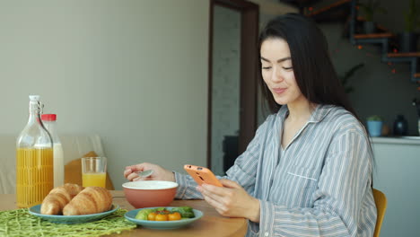 woman eating breakfast and using phone at home