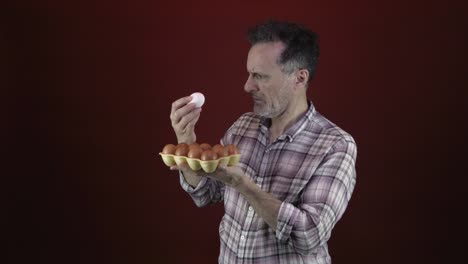 a senior male carefully examining a white egg while holding a carton of brown eggs