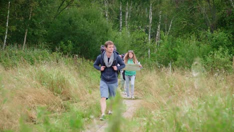 Group-of-tourists-with-backpacks-and-map-walk-along-path-among-dense-thickets