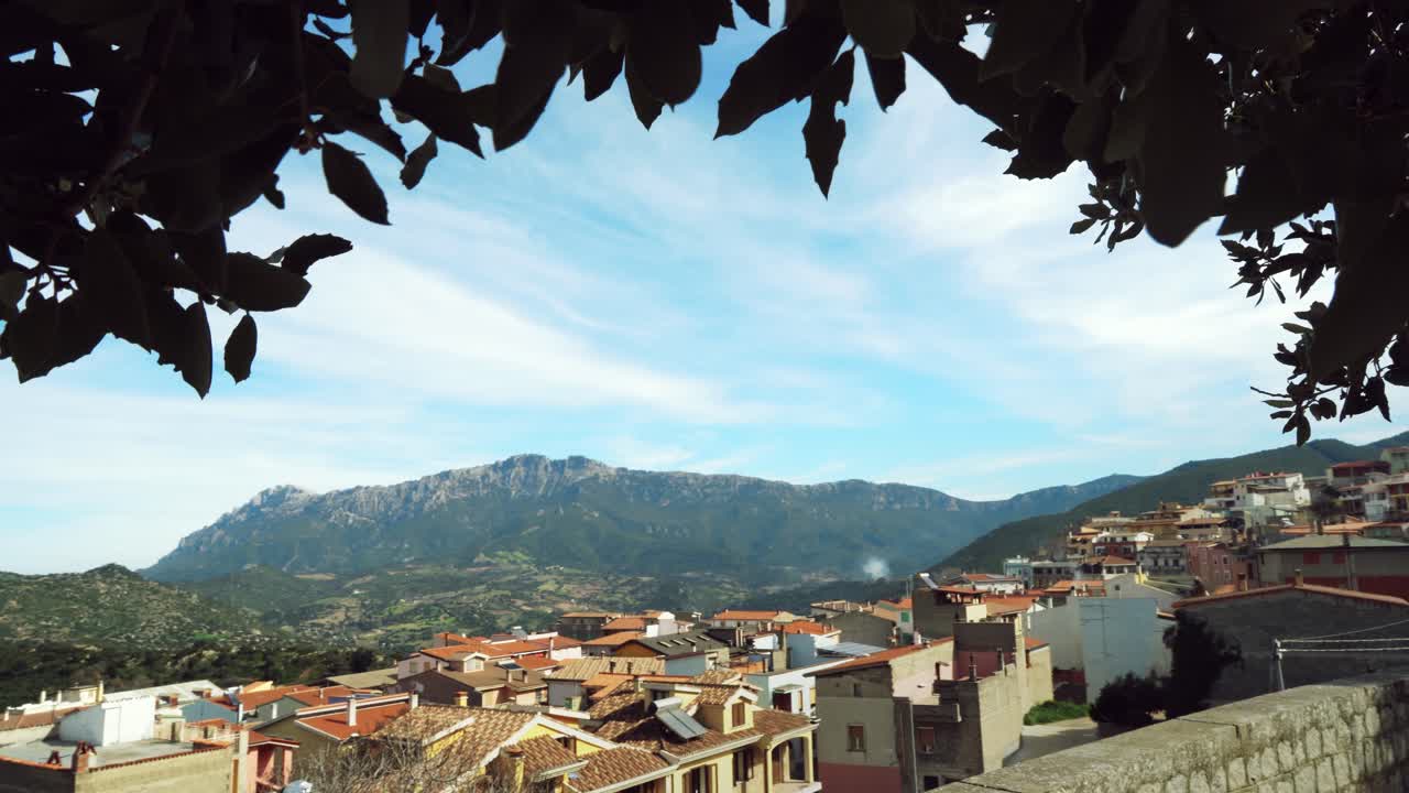 Landscape view of the municipality of Orgosolo, Sardinia in Italy. Leaves in the foreground frame the scene, creating a natural vignette around this Italian town.