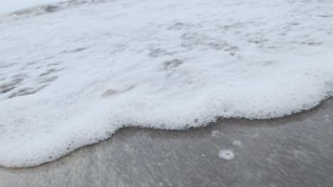 Schaumiges-Meerwasser,-Das-An-Einem-Sandstrand-In-Zeitlupe-Angespült-Wird