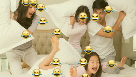 animation of smiling emoji icons over asian parents and two daughters pillow fighting