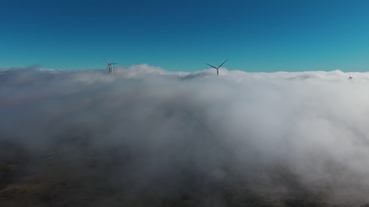 Vista aérea de aerogeneradores emergiendo sobre densas nubes en la isla de Madeira, con una composición minimalista y niebla suave creando una escena atmosférica de energía renovable