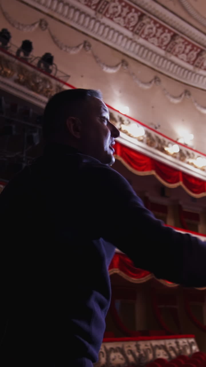 Man talking on a scene of a large theatre. Actor practising on stage before the performance in empty auditorium. Back view. Vertical video