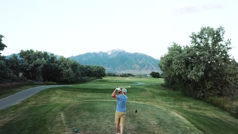 Drohnenschuss,-Der-über-Einen-Mann-Fliegt,-Während-Er-Auf-Dem-Abschlag-Steht-Und-Den-Ball-Ins-Fairway-Treibt