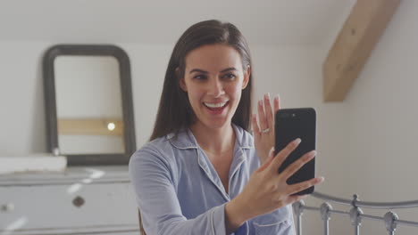 excited woman with mobile phone wearing pyjamas showing engagement ring video chat