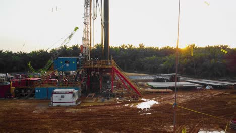 Cinematic-4K-Drone-Footage-of-Onshore-Drilling-Rig-equipment-structure-for-oil-exploration-and-exploitation-in-the-middle-of-jungle-surrounded-by-palm-oil-trees-during-sunset-and-high-oil-price