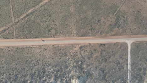 Coche-Conduciendo-Por-Una-Carretera-Rural-En-El-Desierto-Australiano-Con-Una-Larga-Sombra-Durante-La-Hora-Dorada-En-Exmouth,-Australia-Occidental