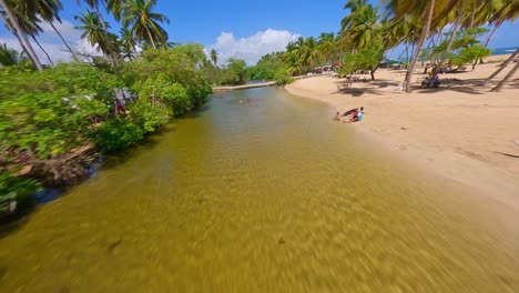 Vuelo-De-Drones-Fpv-A-Lo-Largo-De-La-Playa-De-Arena-Y-El-Río-Con-Niños-Jugando-En-Arroyo-Saldo-Durante-El-Verano