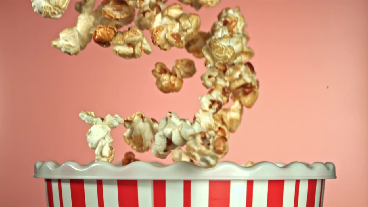 Popcorn che cadono al rallentatore in un secchiello per popcorn a strisce