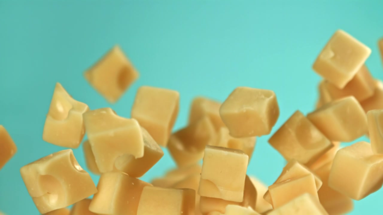 Cubes de fromage en chute au ralenti sur un fond sarcelle