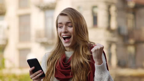 Cheerful-woman-jumping-with-phone.-Excited-girl-looking-cellphone-on-street.
