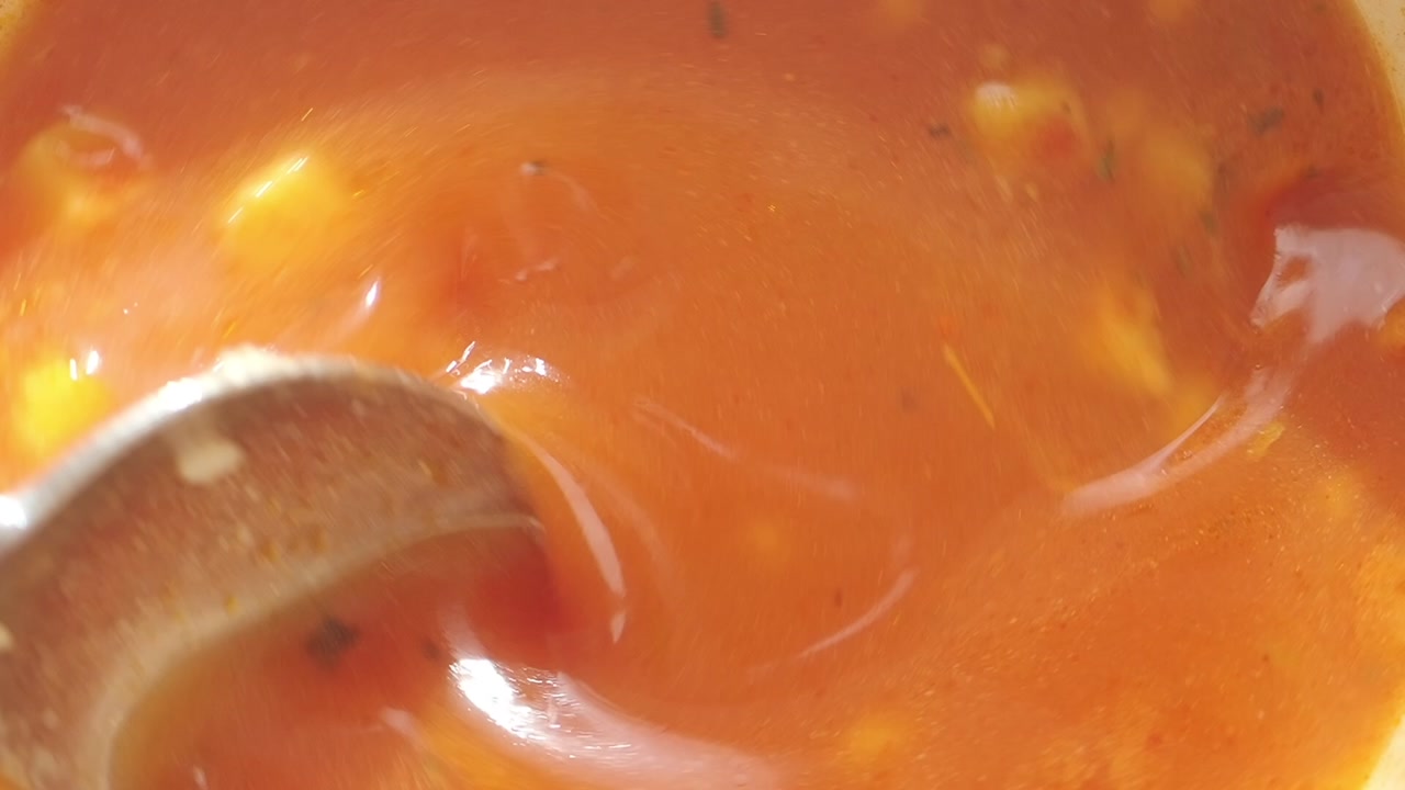 Close-Up of Spoon Stirring Hot Tomato Soup with Vegetables