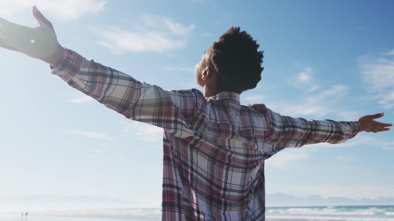 African american woman with arms wide at the beach on sunny day