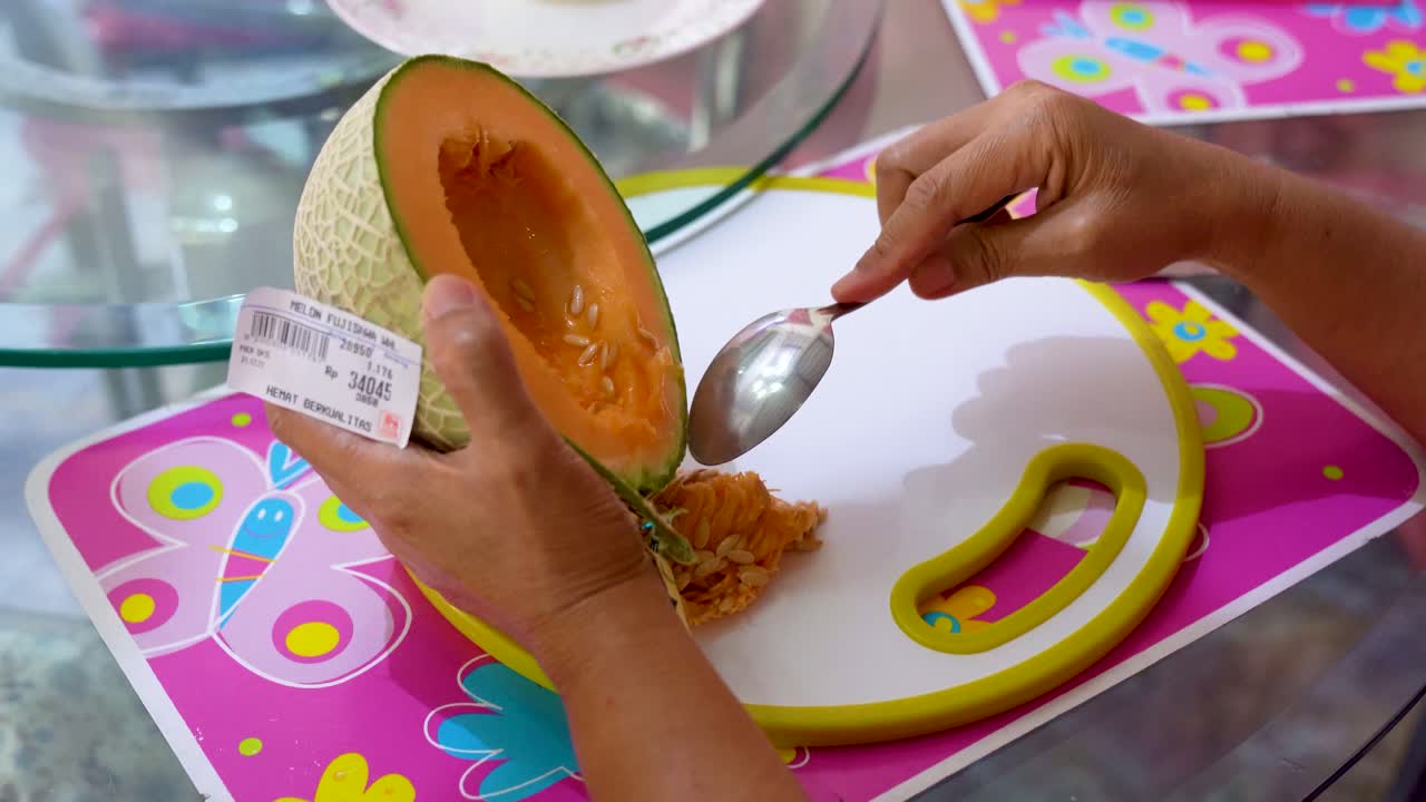 Hands of woman use spoon to clean and remove seeds from golden melon
