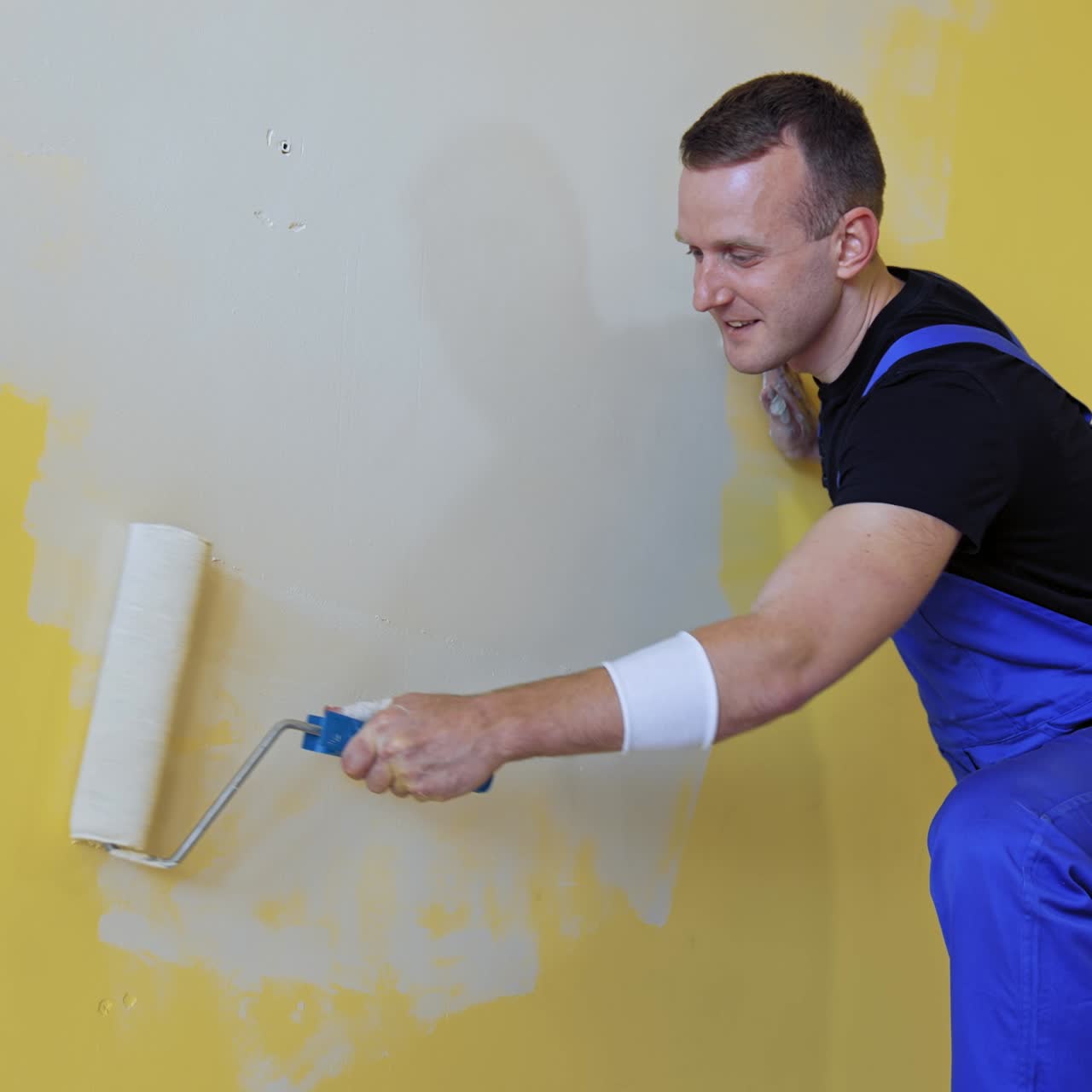 Man making repairs in new flat. Young man painting wall with roller brush while renovating his apartment