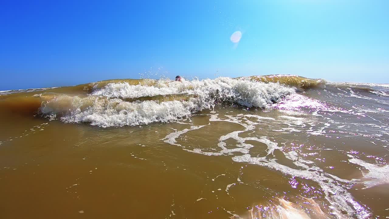 Boy enjoys in waves in the sea. Cute child jumping into big waves with white foam in a sunny summer day. Happy childhood.