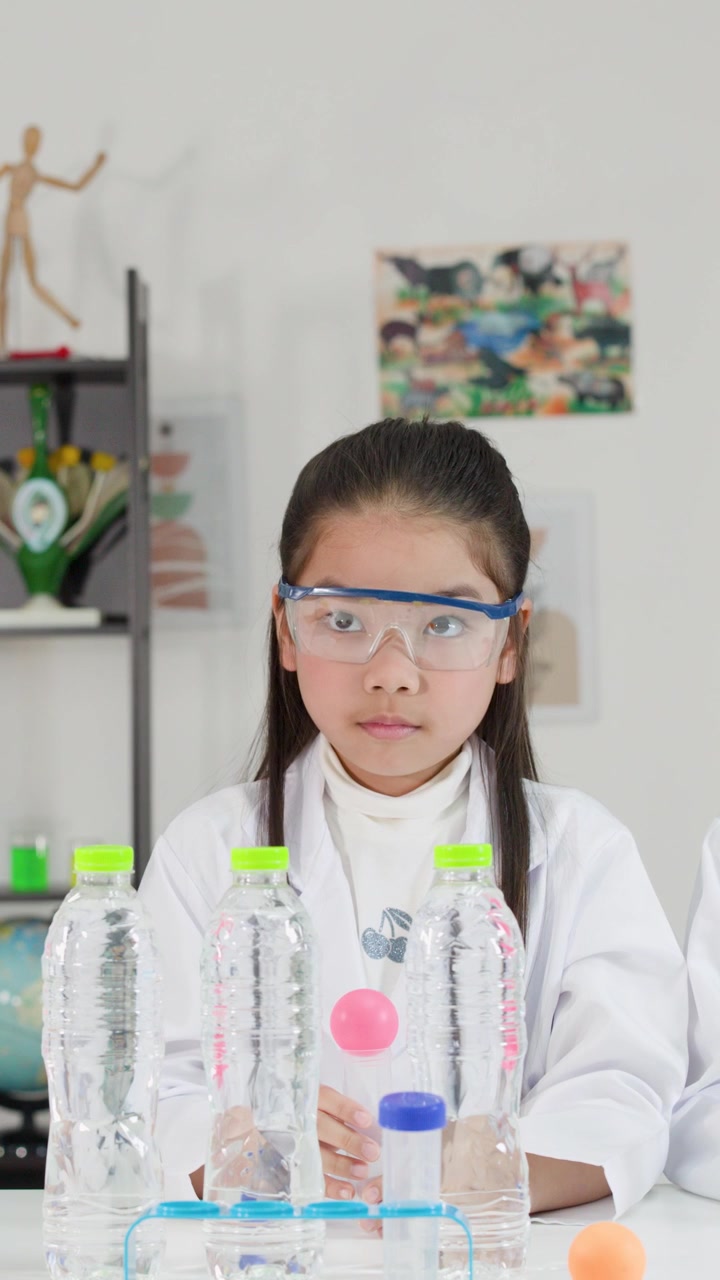 Mahasiswa Asia mengenakan jas lab melakukan percobaan prinsip Bernoulli menggunakan tekanan udara dan botol.