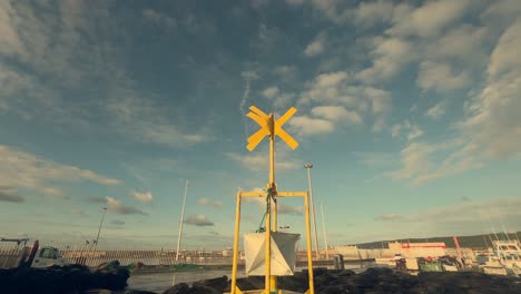 Una-Boya-De-Navegación-Amarilla-Se-Alza-Orgullosa-En-El-Muelle-De-Un-Pueblo-Pesquero-Costero-Español,-Simbolizando-La-Seguridad-Marítima-Y-La-Orientación-En-Medio-De-Las-Bulliciosas-Actividades-Del-Puerto.