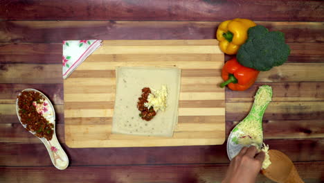 a top view of spreading cheese and mince for spring roll, two big yellow and red capsicums and a green broccoli on the table